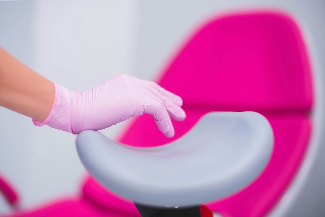 A gynecologist doctor in pink gloves holds his hand close-up on the background of a gynecological chair. Nurse in pink gloves at the clinic. female medicine. women Health. gynecologist in pink gloves