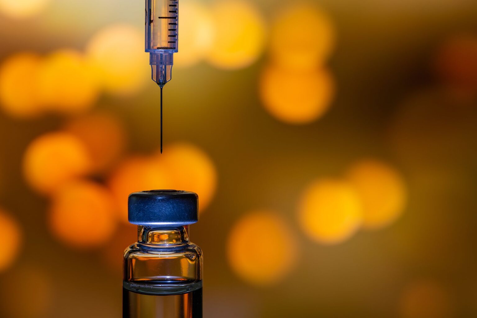 A syringe with the needle point to the vaccine vial on the colorful abstract background